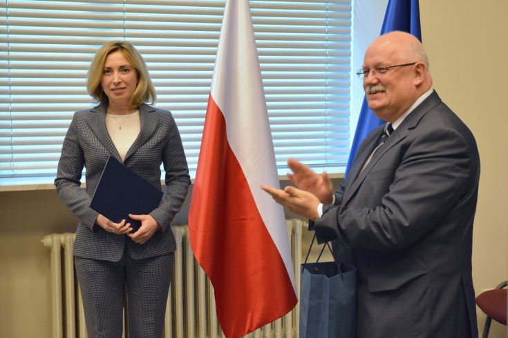 Na tle flag Polski i UE stoją: Iryna Vereshchuk - trzyma teczkę z certyfikatem i Dyrektor KSAP - klaszcze.